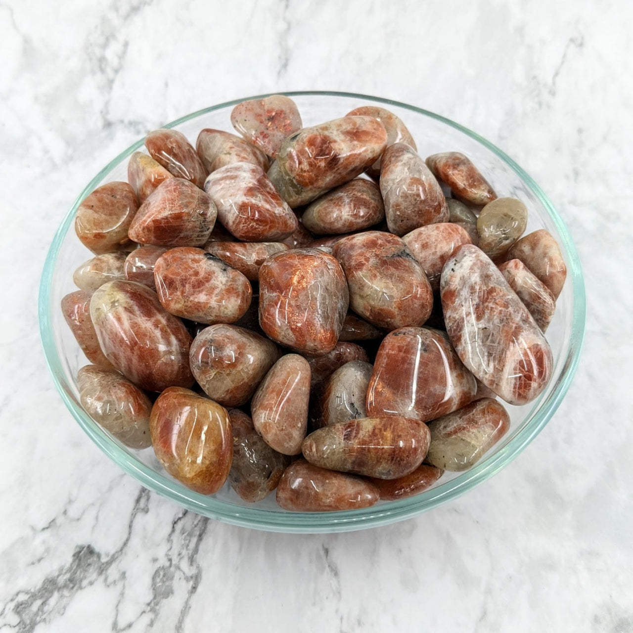 A bowl of Sunstone Grade A tumbled stones featuring red and white marble rocks