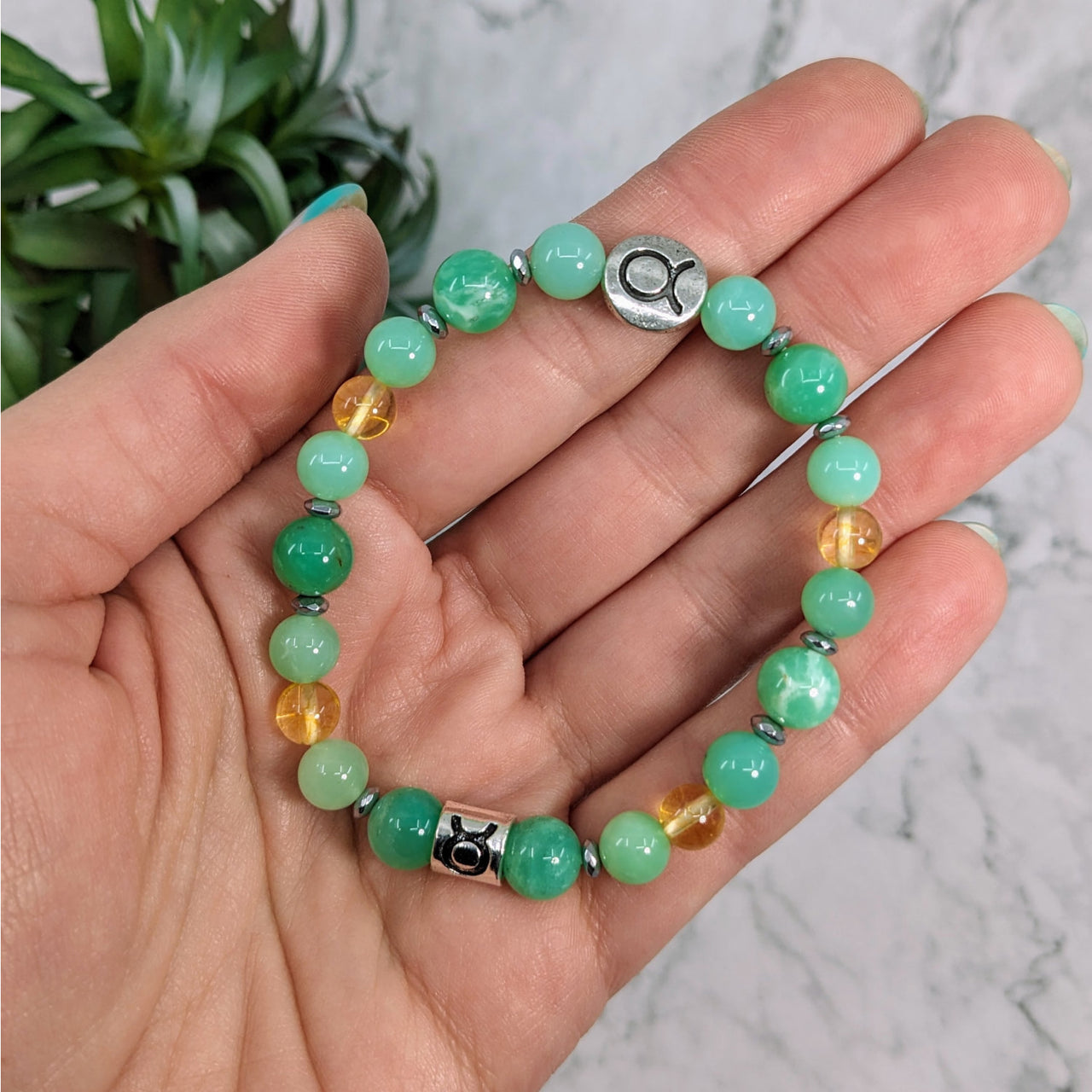 Hand holding Taurus Zodiac Handmade Beaded Bracelet with green beads and silver clasp jewelry