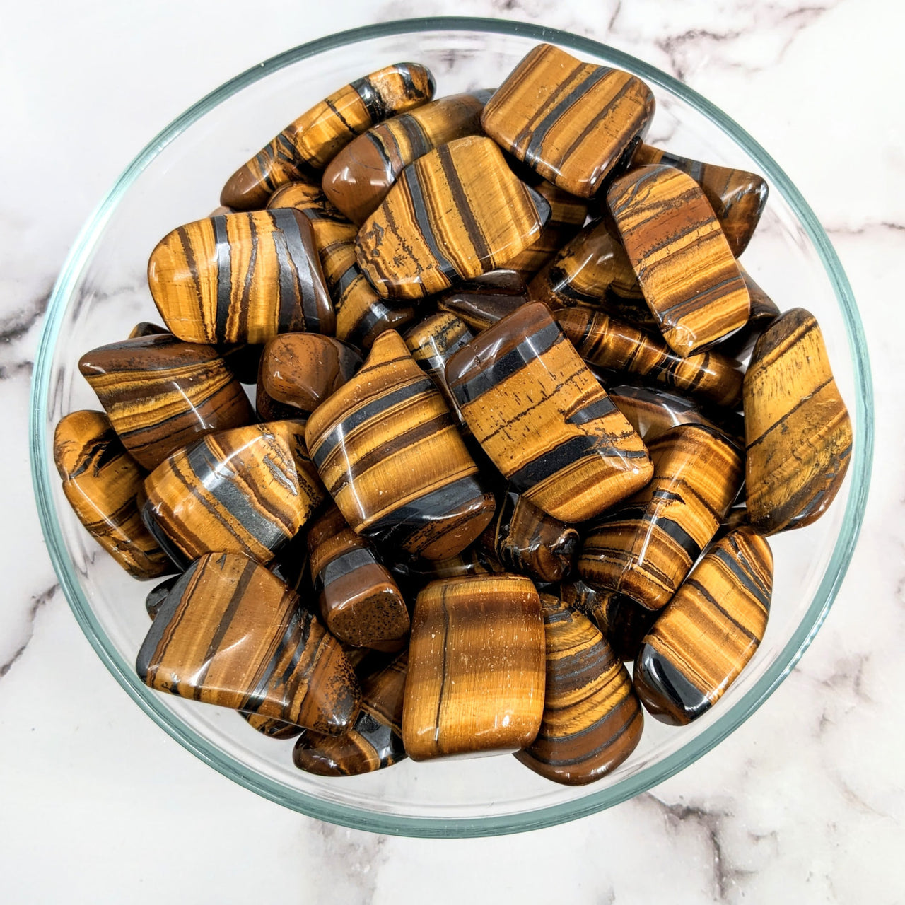 A bowl filled with chocolate covered chocolates next to Tiger’s Eye tumbled stones