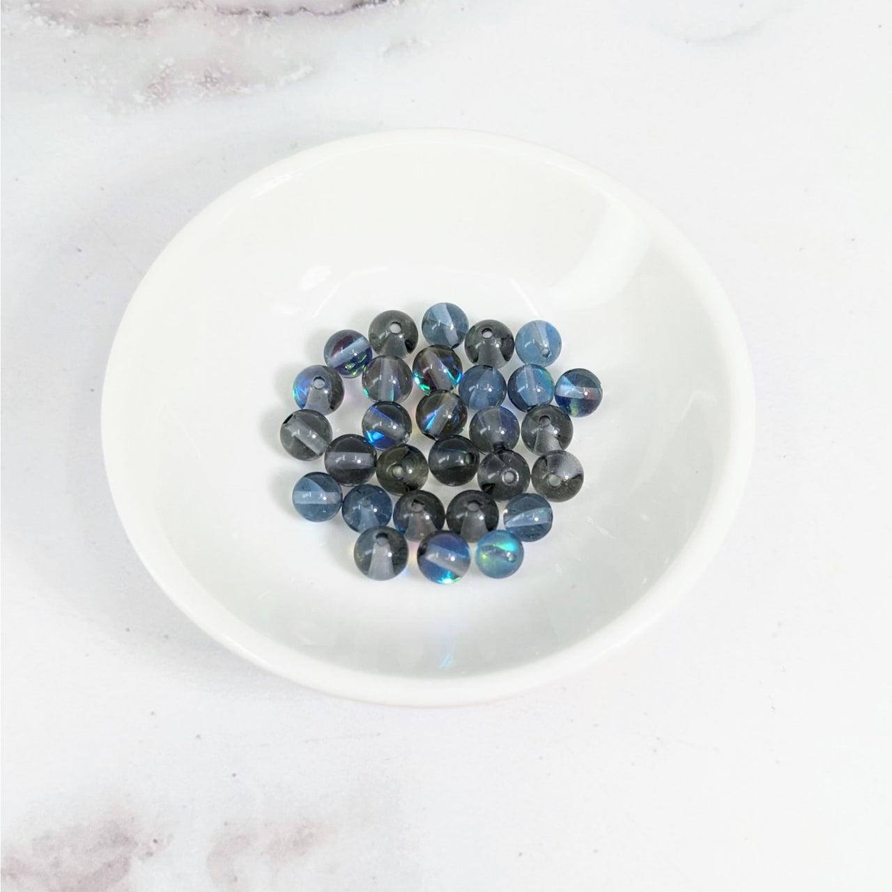 White bowl of blue and black marble beads from Titanium Aura Quartz 6 mm Round Bead pack LV3625