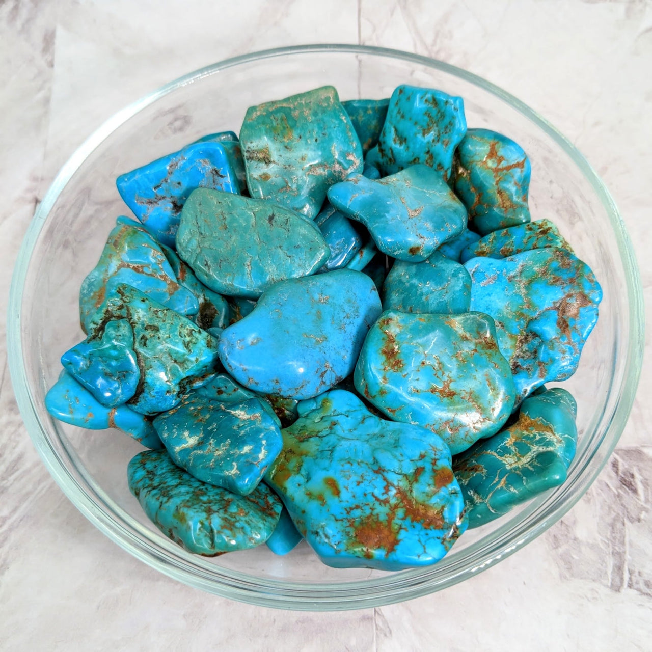 Close-up of Turquoise Wavy Semi Polished rocks in a bowl on a table - Product #LV2254