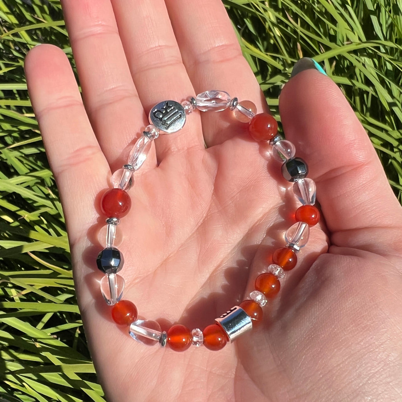 Hand holding Virgo Zodiac handmade beaded bracelet with red and black beads, 7’ long