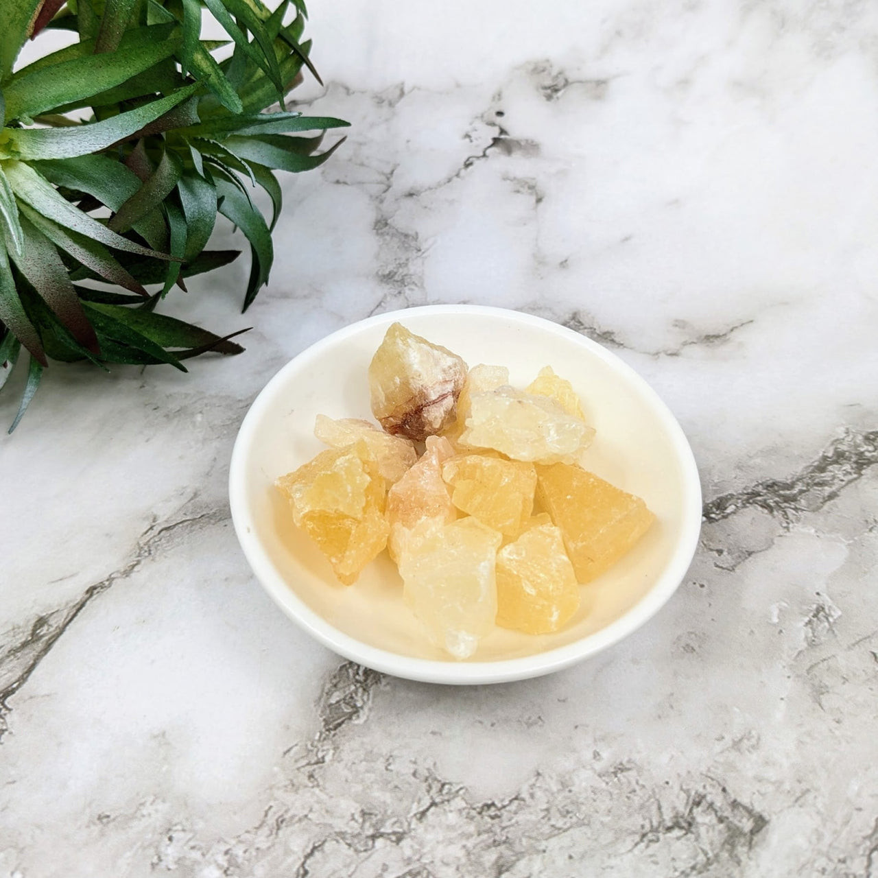 Bowl of fruit on marble table with plant, showcasing Yellow Calcite Small.7 - 1’ Bulk Lot #LV4091